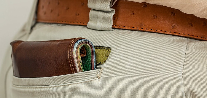 A brown wallet poking out of the back pocket of a pair of beige jeans