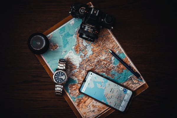 A Map upon which has been placed A Digital Camera a Watch, A Mobile Phone and a Compass. All designed to show Travel for the article - Top Tips for Succesful International Travel by Futureyousuccess.com