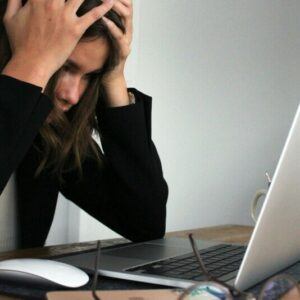  A girl sitting with her head in her hands, looking in despair as she looks at an open laptop, trying to decide what to do next.