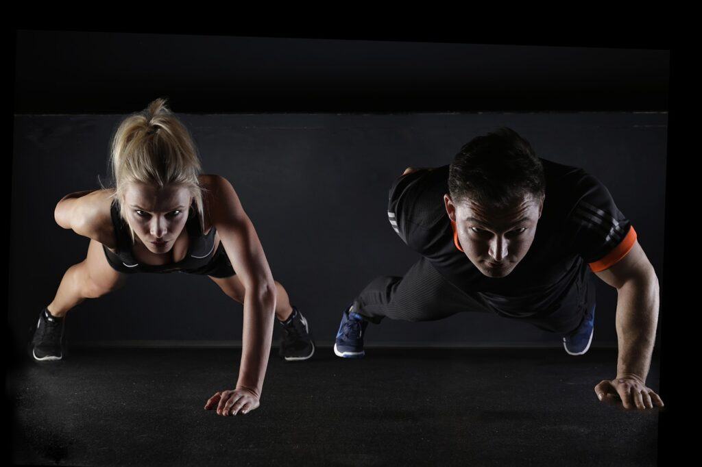 A Man and Woman facing the camera head on, both wearing gym gear in a dark moody setting and both in a one armed press up position. The image is to back up the article by Future You Success on Burn Fat - Best Exercise to Lose Belly Fat and that Abdominal Exercises are one of the best exercises to Burn Fat