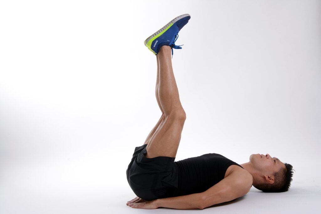 A man in gym gear, laying on his back on the floor. his arms are straight beside him and his legs are raised off the floor at near 90 degrees to his torso performing a leg raise in conjunction with the description of leg raises in the article Burn Fat - The Best Exercise to Lose Belly Fat by Future You Success