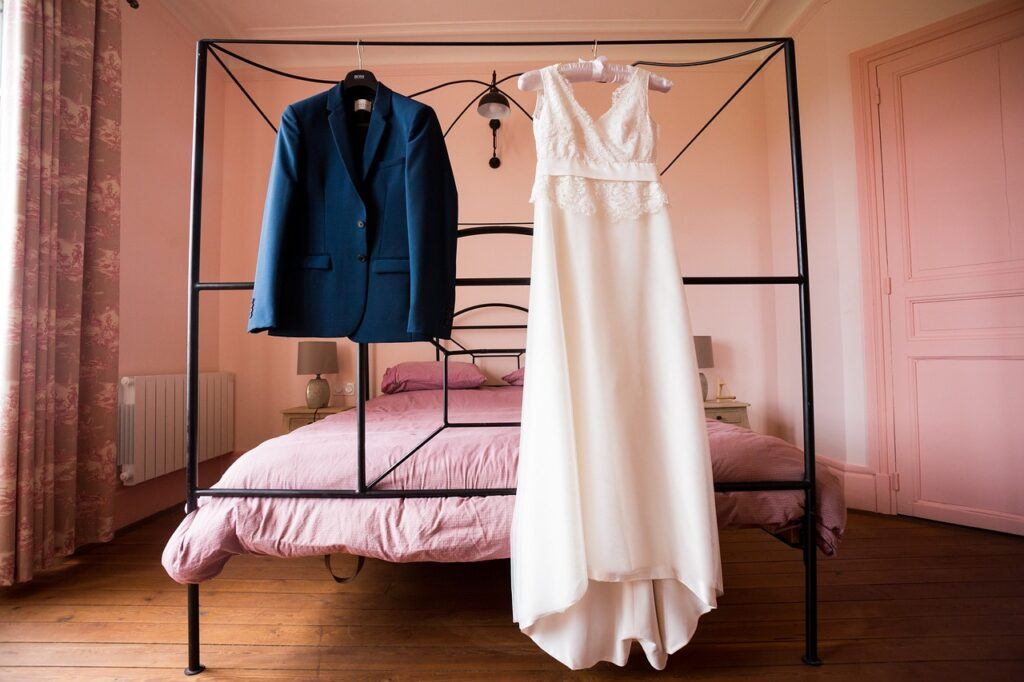 How to Pack Clothes So They Don't Wrinkle - A smart Blue Blazer and a pale pink shoulderless dress hanging up on the top rails of a metal four poster bed